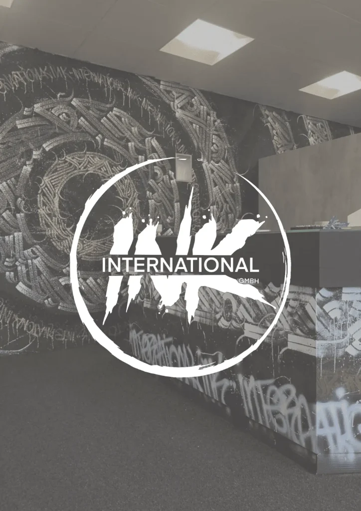 International-Ink GmbH Logo inmitten eines kreativen Kunstwerks mit vielfältigen Tattoomotiven auf der Ladentheke im Hintergrund. Erleben Sie erstklassige Tattoo-Kunst und eine einzigartige Auswahl an Motiven in unserem Studio. Kunst, Kreativität und handwerkliches Können vereint für unvergessliche Tattooerlebnisse. Entdecken Sie unsere exklusiven Designs und lassen Sie sich von unserem Talent inspirieren.